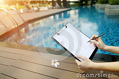 Focus on document, girl fills empty paper on background of pool. Front used with Open Font License Stock Photo