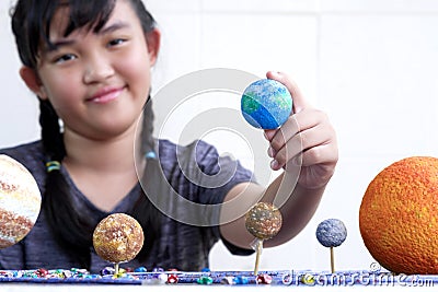 Focus at girl hand holding earth planet with blurred background, young smiling Asian girl showing her homemade solar system model Stock Photo