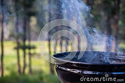 Focus on a portable charcoal grill at a campsite overlooking a green forest Stock Photo