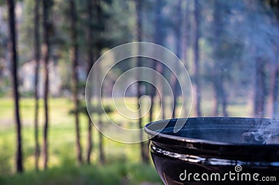 Focus on a portable charcoal grill at a campsite overlooking a green forest Stock Photo