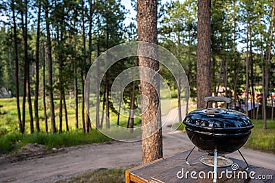 Focus on a portable charcoal grill at a campsite overlooking a green forest Stock Photo