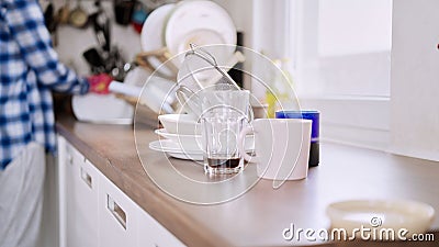 Focus shot of a pile dirty dishes on a kitchen counter with a person standing in the background. Stock Photo