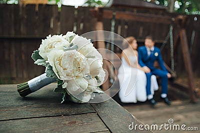 In focus wedding bouquet on a wooden floor against a background of kissing newlyweds. Wedding concept Stock Photo