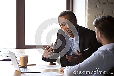 Diverse employees negotiate gesturing near laptop in office Stock Photo