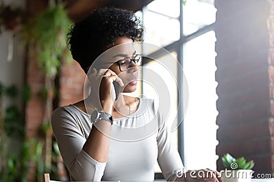 Pensive biracial female busy talking on cellphone at work Stock Photo