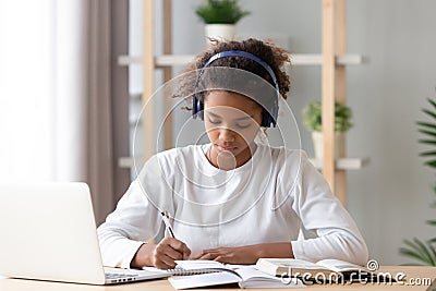 Focused african african teen girl wearing headphones writing notes studying Stock Photo