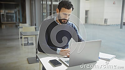 Focused bearded man working on laptop in modern office, showing professionalism and concentration Stock Photo