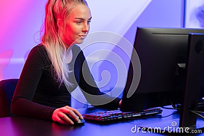 Focused Blonde Gamer Girl Playing Online Video Game on Her Personal Computer. Stock Photo