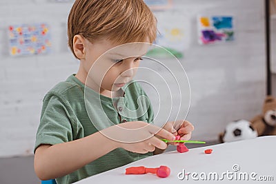 focused boy with colorful plasticine sculpturing figure at table Stock Photo