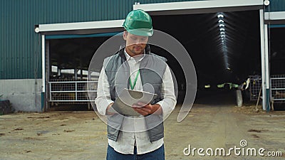 Focused engineer making notes at modern cowshed building in protective helmet. Stock Photo
