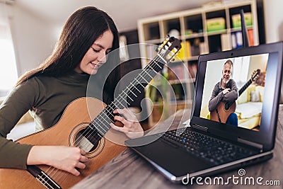 Girl playing acoustic guitar and watching online course on laptop while practicing at home. Online training, online Stock Photo