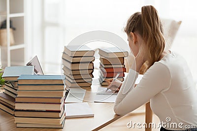 Focused girl writing in notebook surrounded by books at table Stock Photo