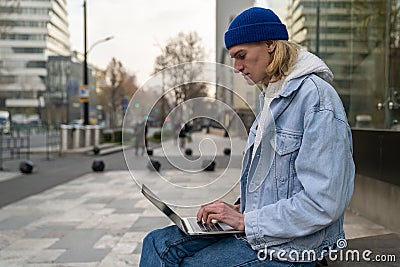Focused guy freelancer doing urgent work on laptop on street sitting on bench in downtown. Stock Photo
