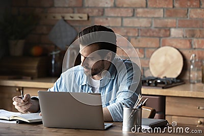 Focused guy take notes sitting by laptop at kitchen table Stock Photo