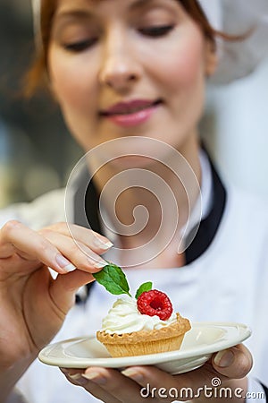 Focused head chef putting mint leaf on little cake on plate Stock Photo