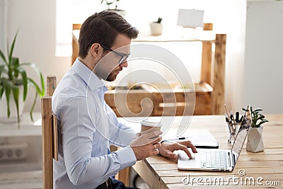 Focused male employee working at laptop drinking coffee Stock Photo