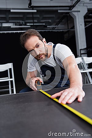 Focused male craftsman in working overall making measurements of floor by Stock Photo
