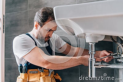 Focused male plumber in working overall fixing sink Stock Photo