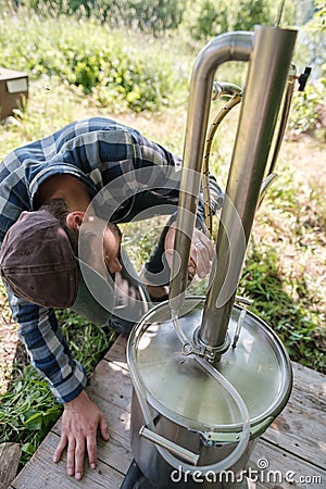 Focused man makes an alcohol mashine in a village courtyard, on a summer day. Preparation of an alcoholic beverage. Stock Photo