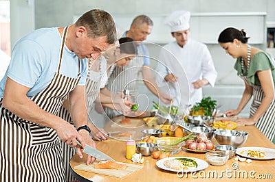 Focused man cutting fish during group cooking lesson Stock Photo