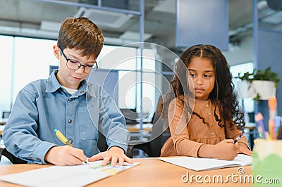 Focused multiracial students kids writing down data into notebook while sitting at table Stock Photo