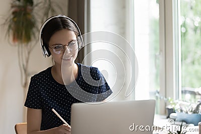 Focused positive young student girl in eyeglasses, headphones writing notes Stock Photo