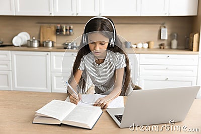 Focused pre teen schoolkid girl in headphones studying from home Stock Photo