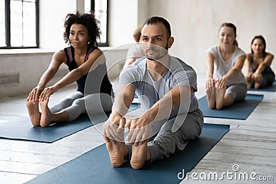 Focused professional male instructor leading yoga class in modern studio. Stock Photo