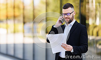 Focused serious businessman lawyer talking by mobile phone with client and reading contract paper Stock Photo