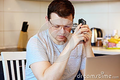 Focused and serious young man in glasses calls on a mobile phone at work sitting at his workplace. Online Job Concept. Self-isolat Stock Photo