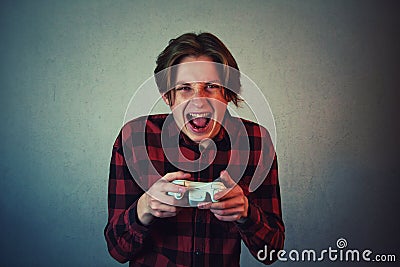 Focused teen boy playing video games isolated on grey wall background. Angry and furious guy holding the joystick console, Stock Photo