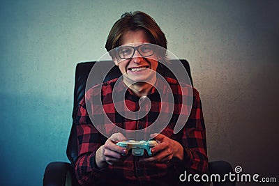 Focused teen boy playing video games late night seated in his chair. Angry and furious guy nerd wearing glasses, holding the Stock Photo