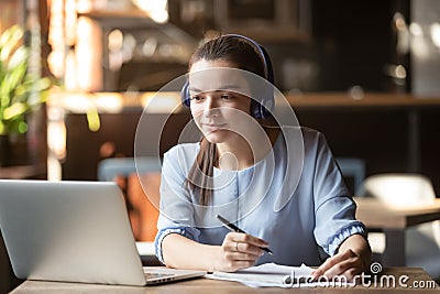 Focused woman wearing headphones using laptop, writing notes Stock Photo