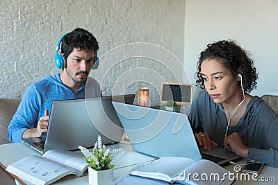 Focused freelancer couple with headphones working and typing in laptop. Inside the house in iving room. Freelance, home Stock Photo