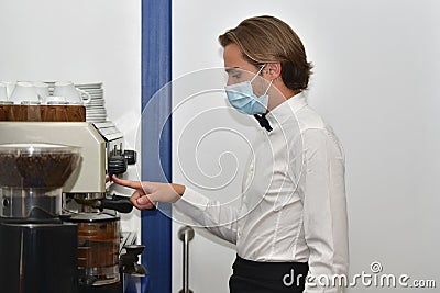young male bartender wearing a surgical mask operating a bar espresso machine. Bartending and safety concept Stock Photo