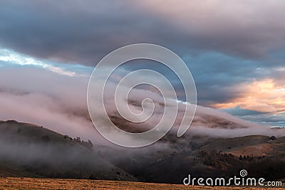 Fog covering some mountains and trees, with warm sunset colors Stock Photo