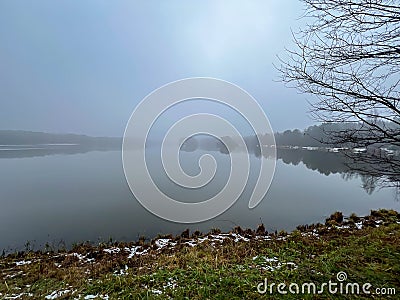 Fog over the surface of the pond occurring in the last days of autumn, creating a gloomy, depressing view but at the same time Stock Photo