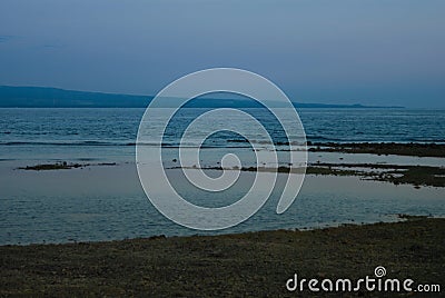 Foggy blue remote shore with pink haze, dark shore and calm sea on sunset, low tide. Tropical indonesian landscape with islands. Stock Photo