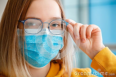 Foggy glasses wearing on young woman. close up portrait. Teenager girl in blue medical protective face mask and eyeglasses wipes Stock Photo