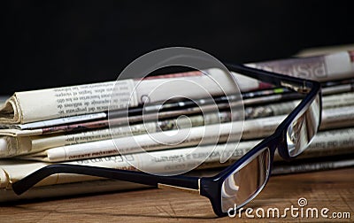 Folded pile newspapers with a pair of blue reading glasses on it Stock Photo