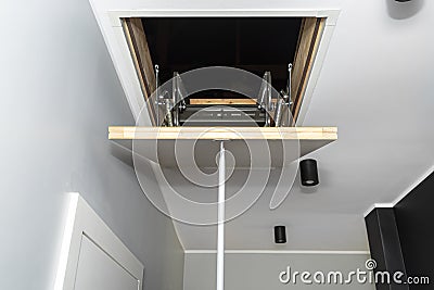 Folding metal stairs to the attic in the ceiling, closed hatch with a tube for opening, modern look. Stock Photo