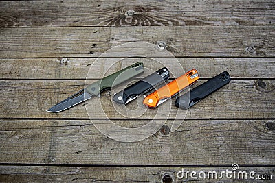 Folding penknives in different colors. Pocket knives for everyday carry. Various knives for hunting, sports and recreation. Wooden Stock Photo