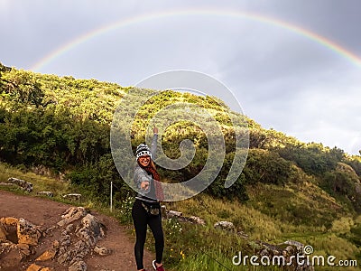 Follow your dream concept. A woman walking along the path to mountain and looking rainbow in the sky. Stock Photo