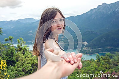 Follow me, Attractive brunette girl holding hands with leads in mountain valley with river Stock Photo