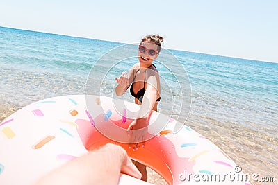 Follow me Vacation concept. woman calls to swim in the sea and waves her hand. Girl relaxing on inflatable ring in the sea. Summer Stock Photo