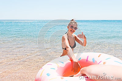 Follow me Vacation concept. woman calls to swim in the sea and waves her hand. Girl relaxing on inflatable ring in the sea. Summer Stock Photo