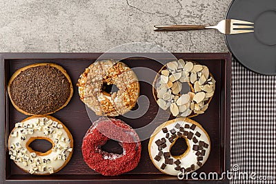 Assortment of donuts on wooden tray with dark plate and small fork and napkin Stock Photo
