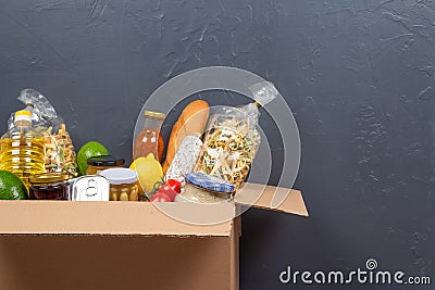 Food bank, food delivery concept. Closeup view of donation box with different food donations on gray wall background Stock Photo