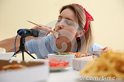Food blogger eating in front of microphone at table against light background. Mukbang vlog Stock Photo