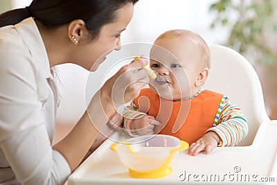 Food, child and parenthood concept - mom with puree and spoon feeding baby at home Stock Photo